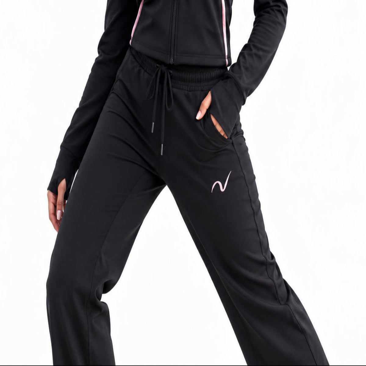 Black athletic jogger pants with a pink wave logo on the thigh, worn by a model outdoors on a gravel path with mountains in the background.
